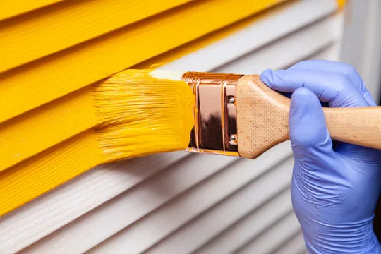 Brushing bright yellow paint onto louvered shutters